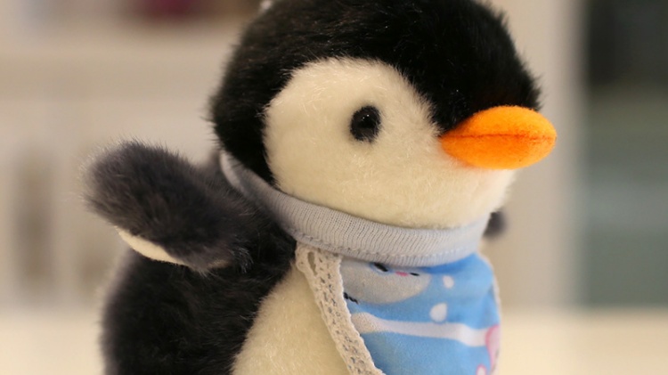 Penguin plush doll wearing blue patchwork bib